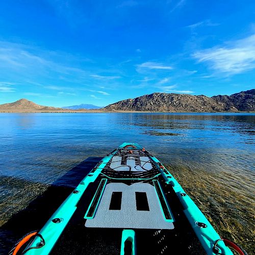 A paddleboard is on clear, calm water with a backdrop of mountains under a blue sky on a sunny day.