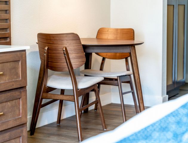 A small wooden table with two wooden chairs in a room with light-colored walls and wooden flooring.