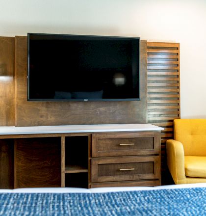 The image shows a modern wooden TV stand with drawers, a flat-screen TV mounted above, and a bright yellow armchair to the right of the stand.