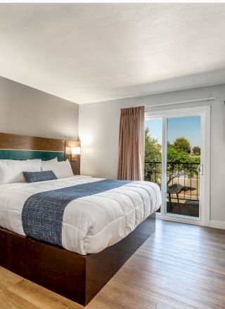 A modern bedroom with wood furniture features a large bed, wall-mounted lamps, a flat-screen TV, and a window with a view, creating a simple design.