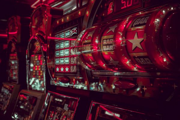 The image depicts a row of illuminated slot machines in a dimly lit casino, featuring the word 