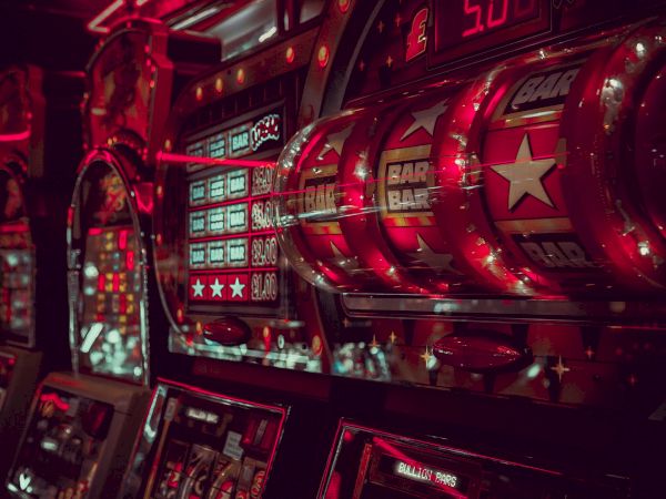 The image depicts a row of illuminated slot machines in a dimly lit casino, featuring the word "BAR" and stars on the reels.