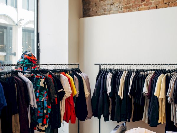 The image depicts a clothing store interior with racks of clothes, folded apparel on tables, large windows, and a brick wall.