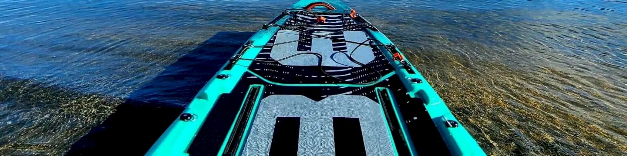 A paddleboard on the shore of a calm lake on a bright day, with mountains and a blue sky in the background ending the sentence.