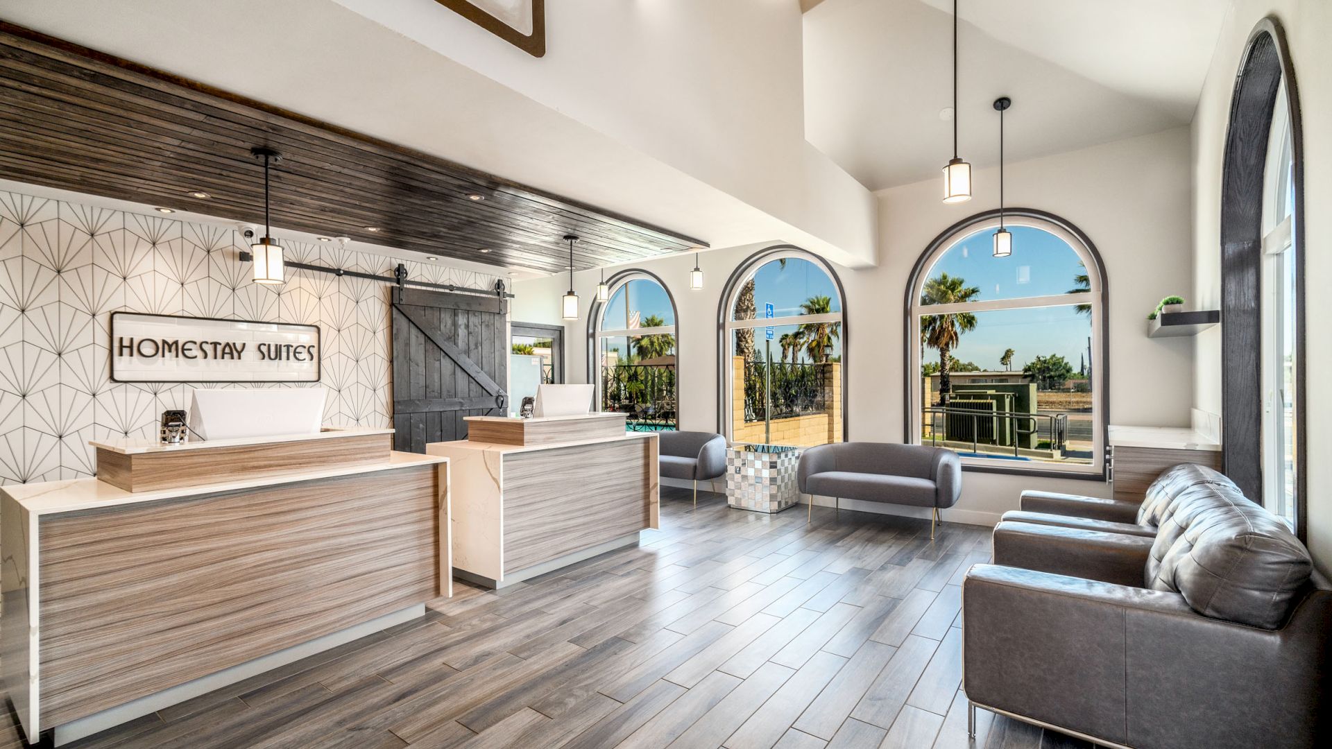 This image shows a modern hotel lobby with minimalist furniture, a reception desk, and large arched windows offering a view of palm trees outside.