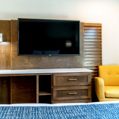 A modern hotel room features a wall-mounted TV, wooden console, and a yellow armchair next to the console.