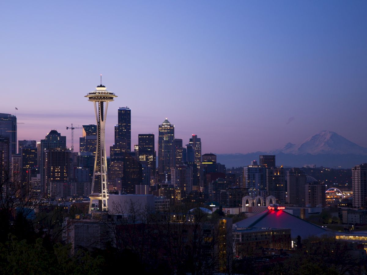 The image shows the Seattle skyline at dusk, featuring the iconic Space Needle, city skyscrapers, and Mount Rainier in the background.