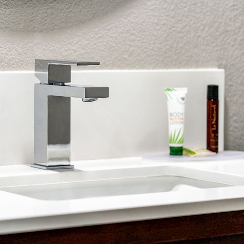 The image shows a modern bathroom sink with a sleek faucet, a tube of cream, and a small brown bottle placed on the countertop.