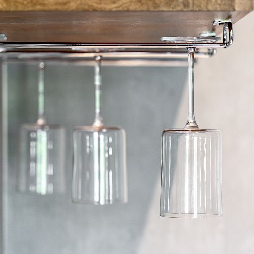 The image shows an under-shelf wine glass rack with empty wine glasses hanging upside down, reflecting off a mirror behind them.