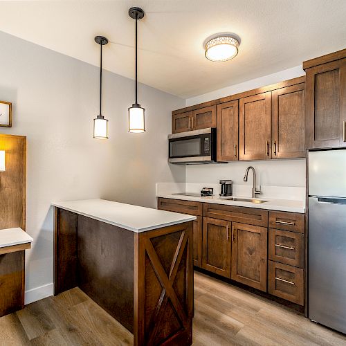 A modern kitchen with wooden cabinets, a small island, pendant lights, and stainless steel appliances. A sign reads 