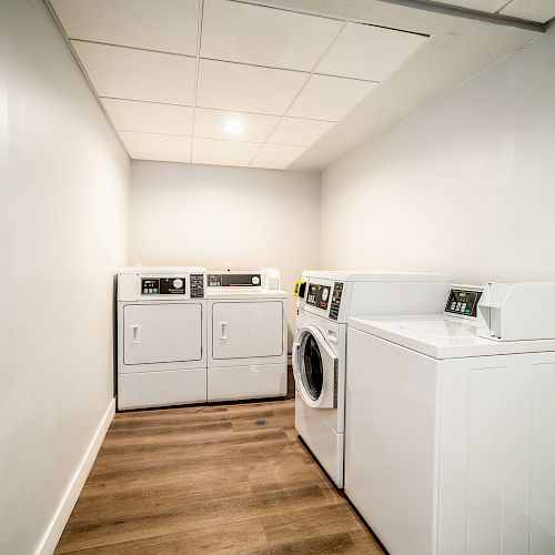 This image shows a laundry room with two washing machines and two dryers, all in white, lined up against the walls under good lighting.