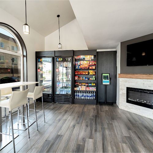 The image shows a modern space with a snack and drink display, high seating area, arched window, a fireplace, and a television mounted on the wall.