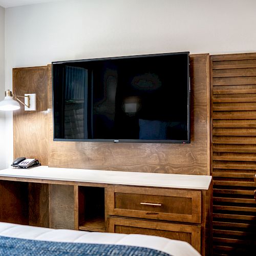 A modern hotel room with a wall-mounted TV, wooden furniture, a phone, and a 