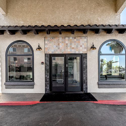 The image shows a building entrance with a double glass door, flanked by two arched windows, and a tiled area above the door.