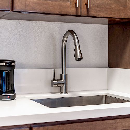 A modern kitchen counter with a stainless steel sink, a sleek faucet, and a coffee maker beside it. Brown cabinets are present above and below.