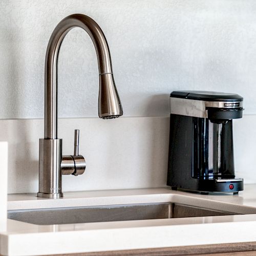 The image shows a modern kitchen with a stainless steel faucet over a sink and a coffee maker on the countertop.