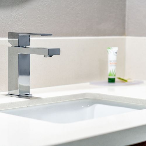 The image shows a modern bathroom sink with a chrome faucet and a tube of toothpaste on the counter.